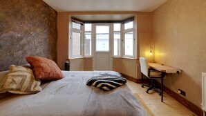 Ein Schlafzimmer mit Bett, Schreibtisch, Stuhl und Erkerfenster mit Blick.