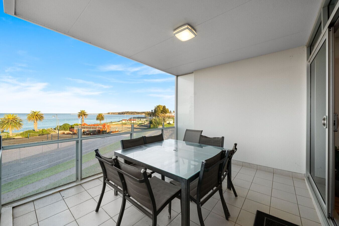 Un balcon avec une table et des chaises en verre, une vue sur la mer et un ciel dégagé.