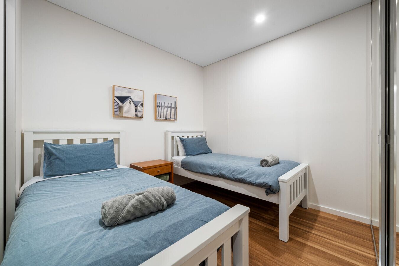 A bedroom with two beds, wooden headboards, a nightstand, and two framed pictures on the wall.