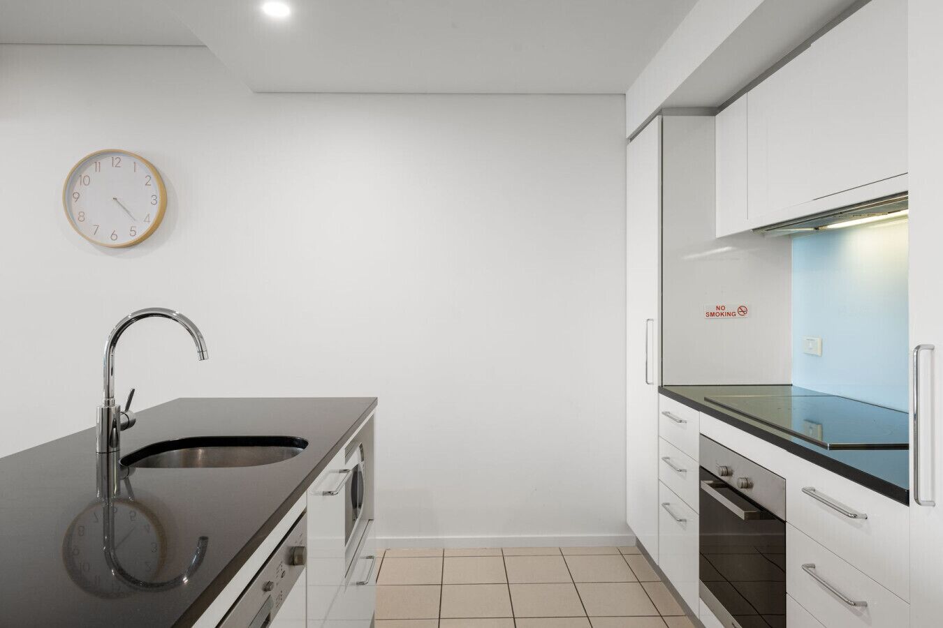 A modern kitchen with a black countertop, stainless steel sink, and a clock on the wall.