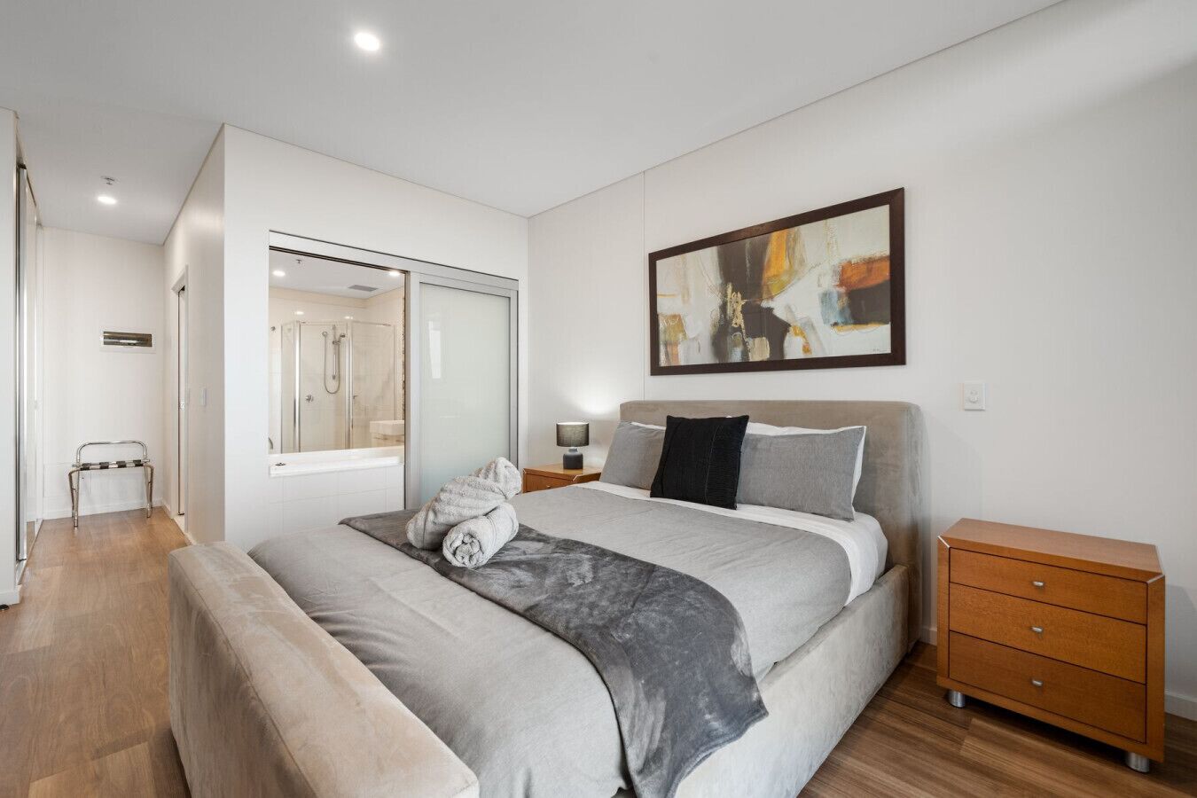 A modern bedroom with a large bed, bedside tables, a nightstand, a glass shower enclosure, and a painting on the wall.