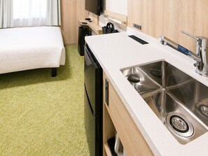 Habitación de hotel compacta con cama, kitchenette y lavamanos.
