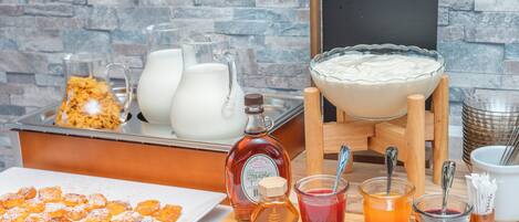 A breakfast buffet with various food items, beverages, and a maple syrup bottle.