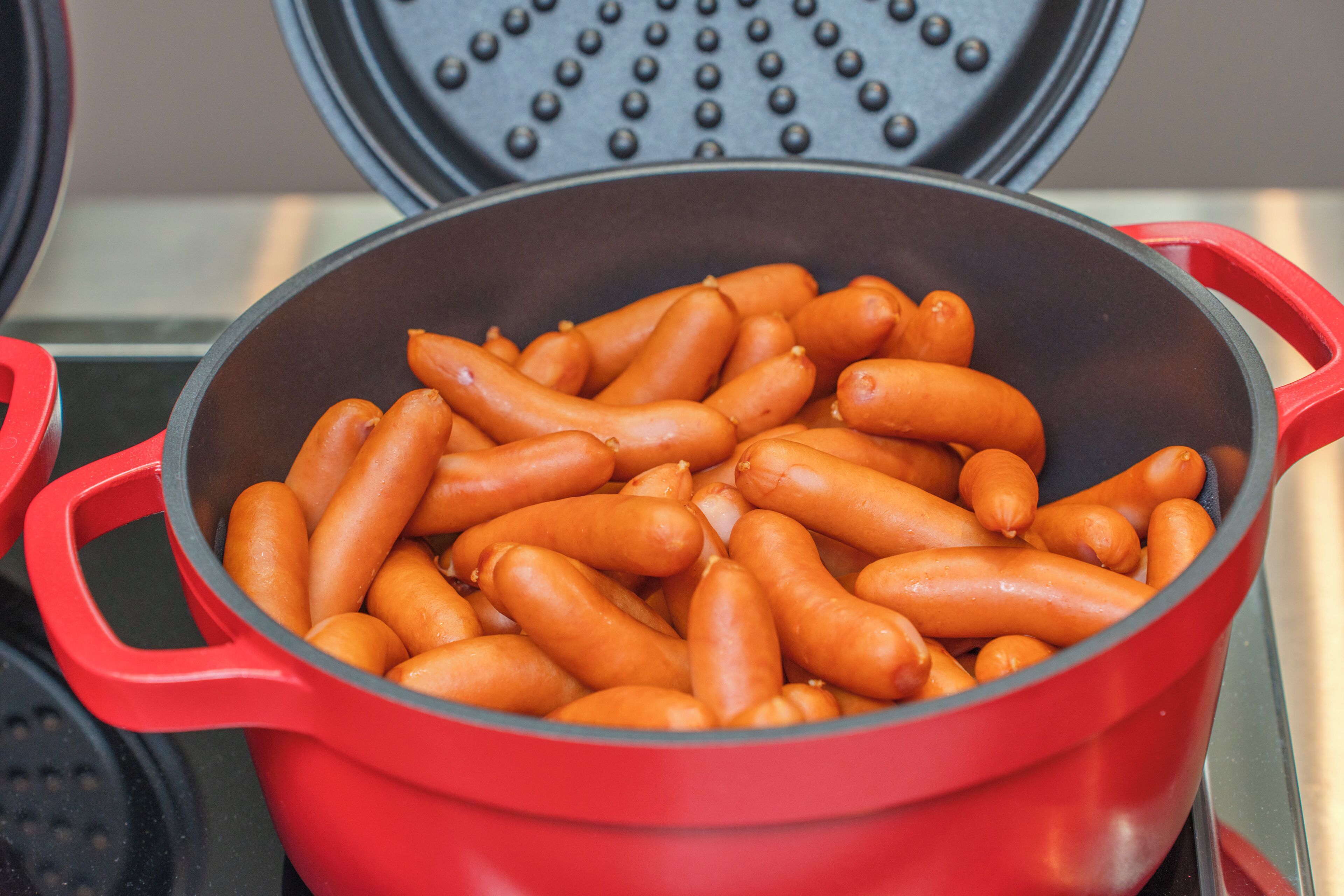 Une cocotte rouge remplie de saucisses, posée sur une cuisinière.