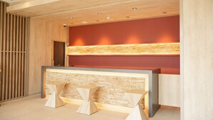 A reception desk with a wooden finish and a stone accent wall, flanked by two geometric stools.