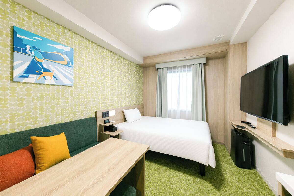 Habitación de hotel con cama, escritorio, televisor y un cuadro en la pared.