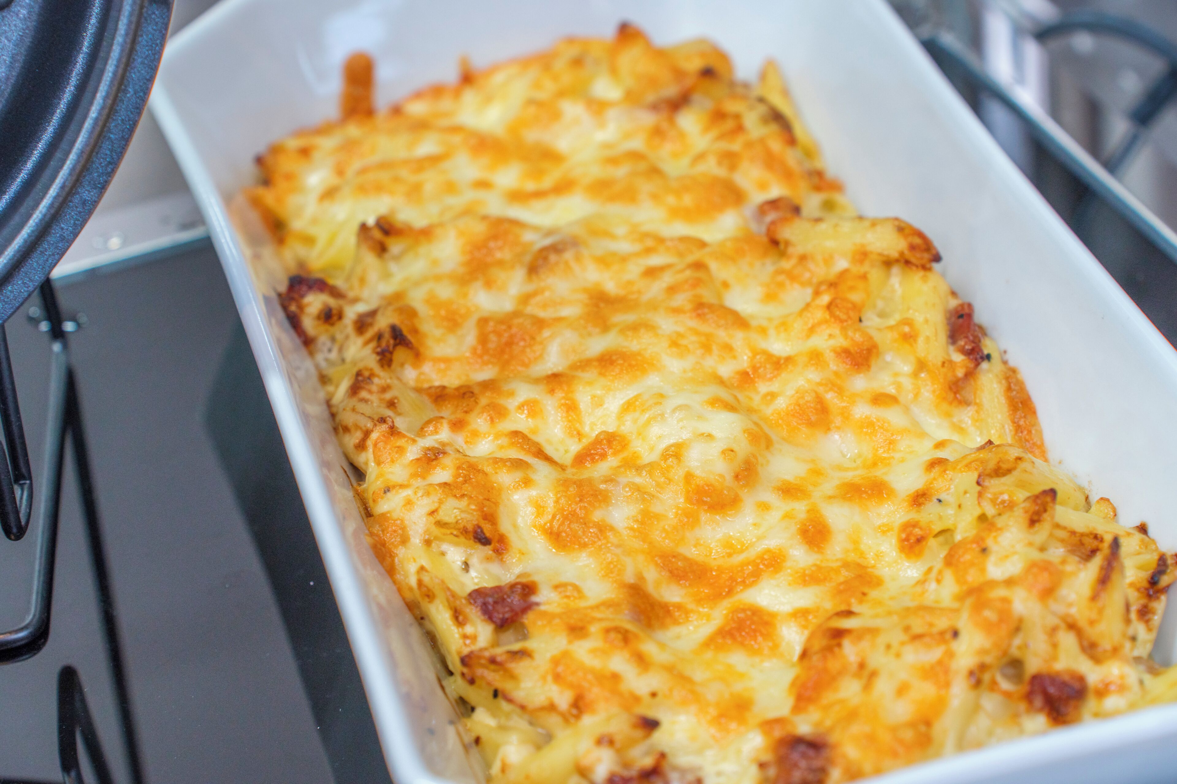 Un plat rectangulaire, probablement en céramique, dans lequel un plat cuit au four, à la croûte dorée, a été préparé. Il pourrait s’agir d’un gratin ou d’un autre plat cuisiné au four.