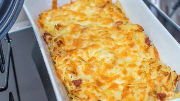 Un plat rectangulaire, probablement en céramique, dans lequel un plat cuit au four, à la croûte dorée, a été préparé. Il pourrait s’agir d’un gratin ou d’un autre plat cuisiné au four.