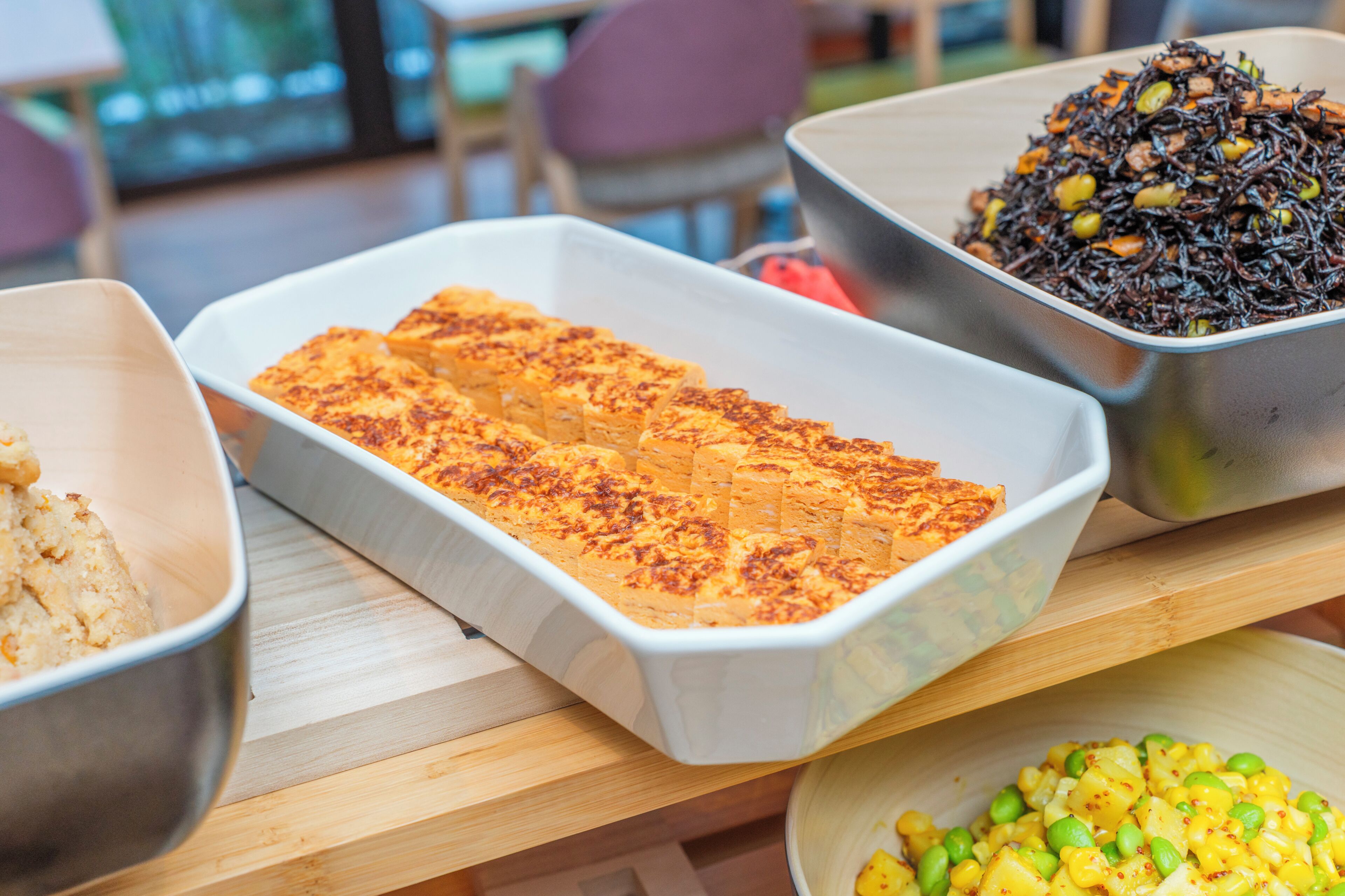 A buffet table with various dishes, including a casserole, a salad, and a dish with black rice.