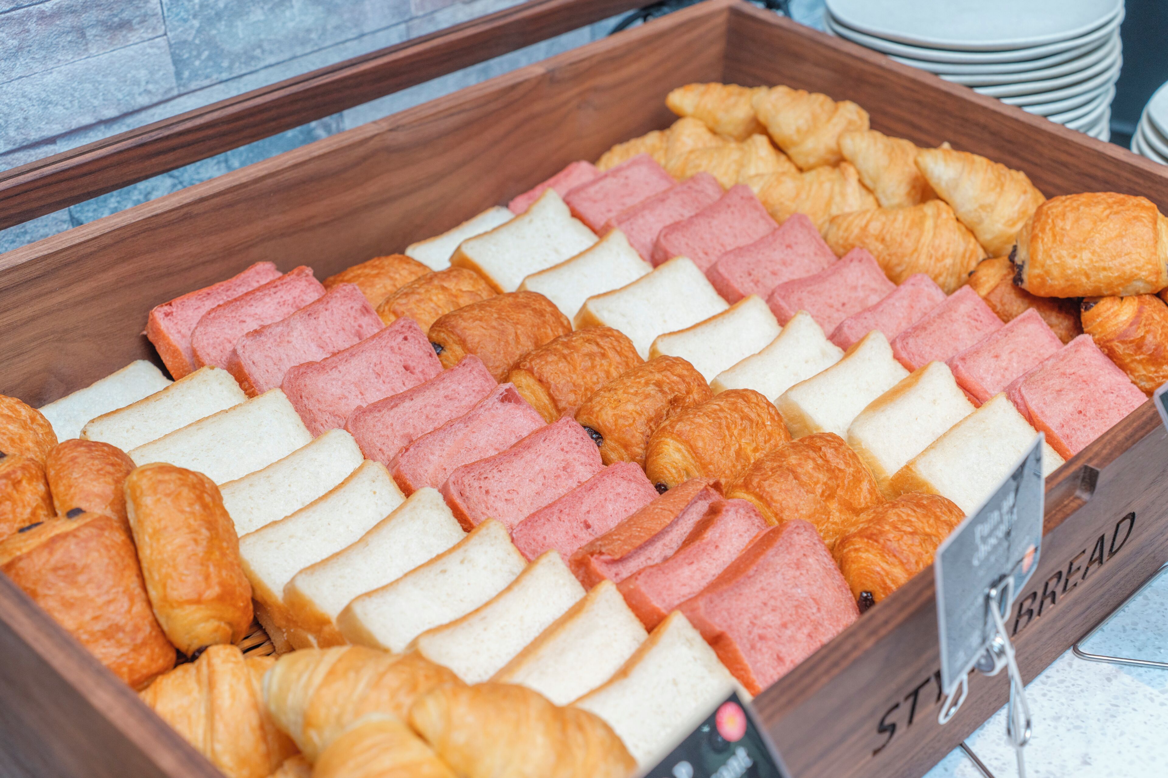 Vitrine de madeira com diversos produtos de panificação, incluindo pão, croissants e doces.
