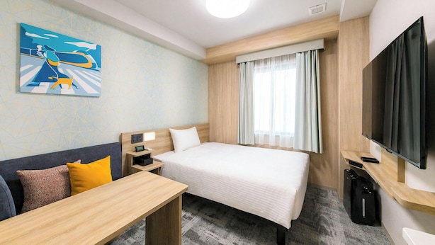 A hotel room with a bed, a desk, a TV, and a painting on the wall.