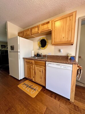 A kitchen with wooden cabinets, a white refrigerator, a dishwasher, a granite countertop, and a sun-shaped decoration on the wall.