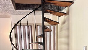 A spiral staircase with metal railings and wooden steps, leading to a ceiling with a textured finish.
