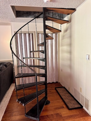 A spiral staircase with metal railings and wooden steps, leading to a ceiling with a textured finish.