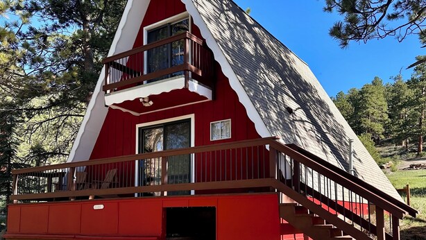 A red cabin with a balcony, a wooden deck, and a clear view of the surrounding trees.