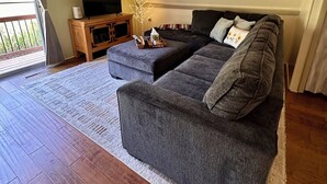 A living room with a grey sofa, a flat-screen TV, a wooden cabinet, and a decorative plant.