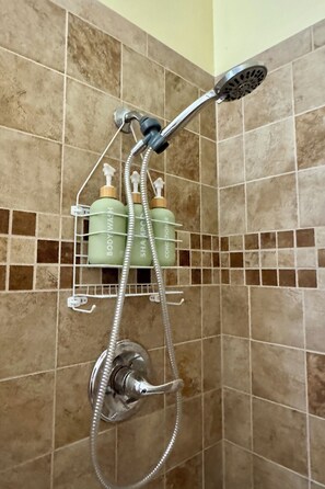 A shower with a handheld showerhead, a wall-mounted faucet, and a soap dispenser rack with bottles.