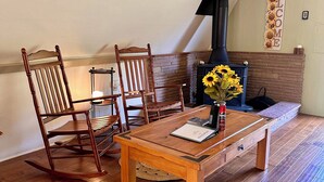 A cozy living room with a wooden table, two rocking chairs, a fireplace, and a 'WELCOME' sign.