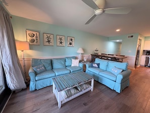 A living room with a sectional sofa, a coffee table, a ceiling fan, and a dining area with a table and chairs.