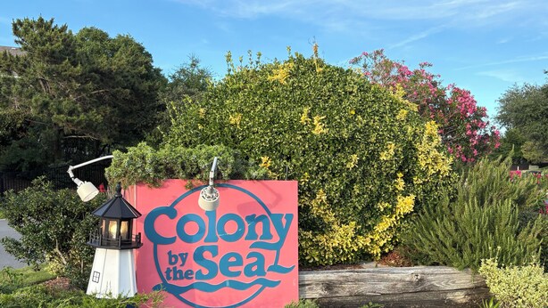 Skilt med teksten 'Colony by the Sea', en lygte og frodigt grønt.