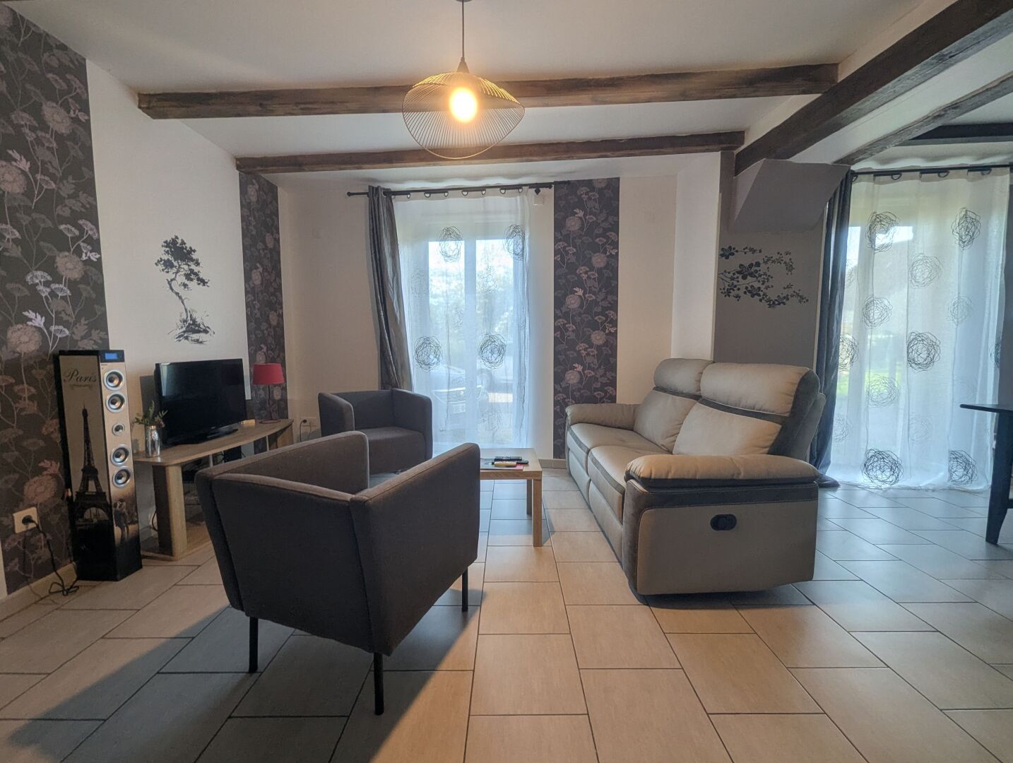 Ein Wohnzimmer mit einer Couch, Sesseln, einem Fernseher und einem dekorativen Poster mit dem Eiffelturm.