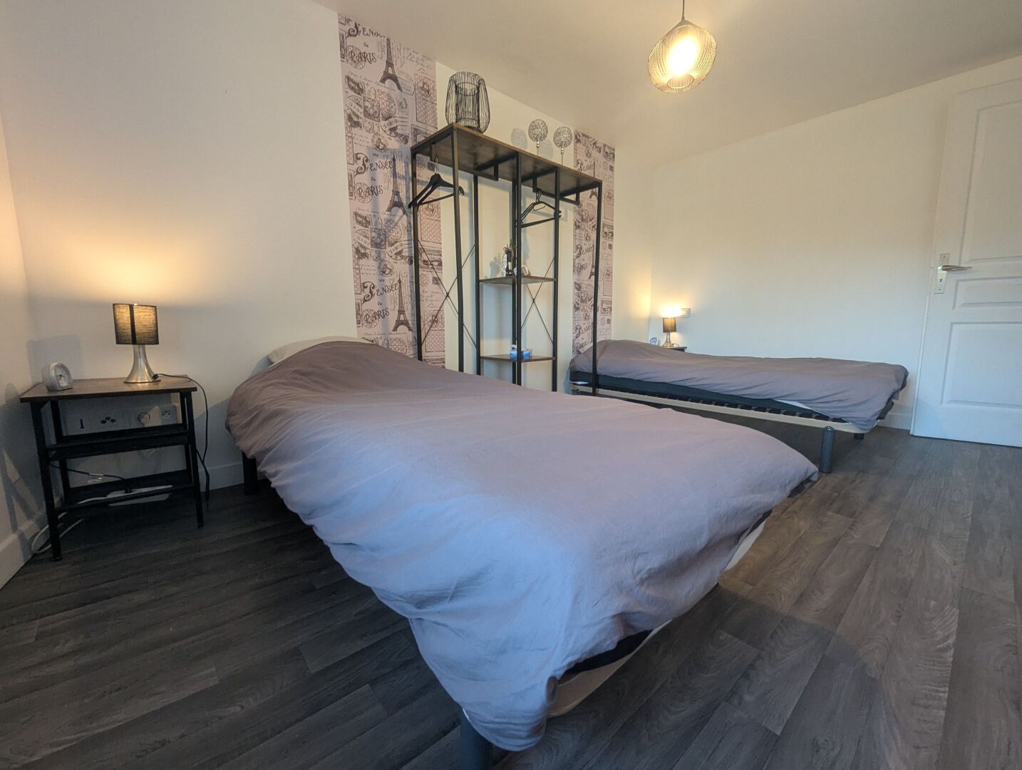 A bedroom with two beds, a bedside table, a lamp, a wardrobe, and a mirror.