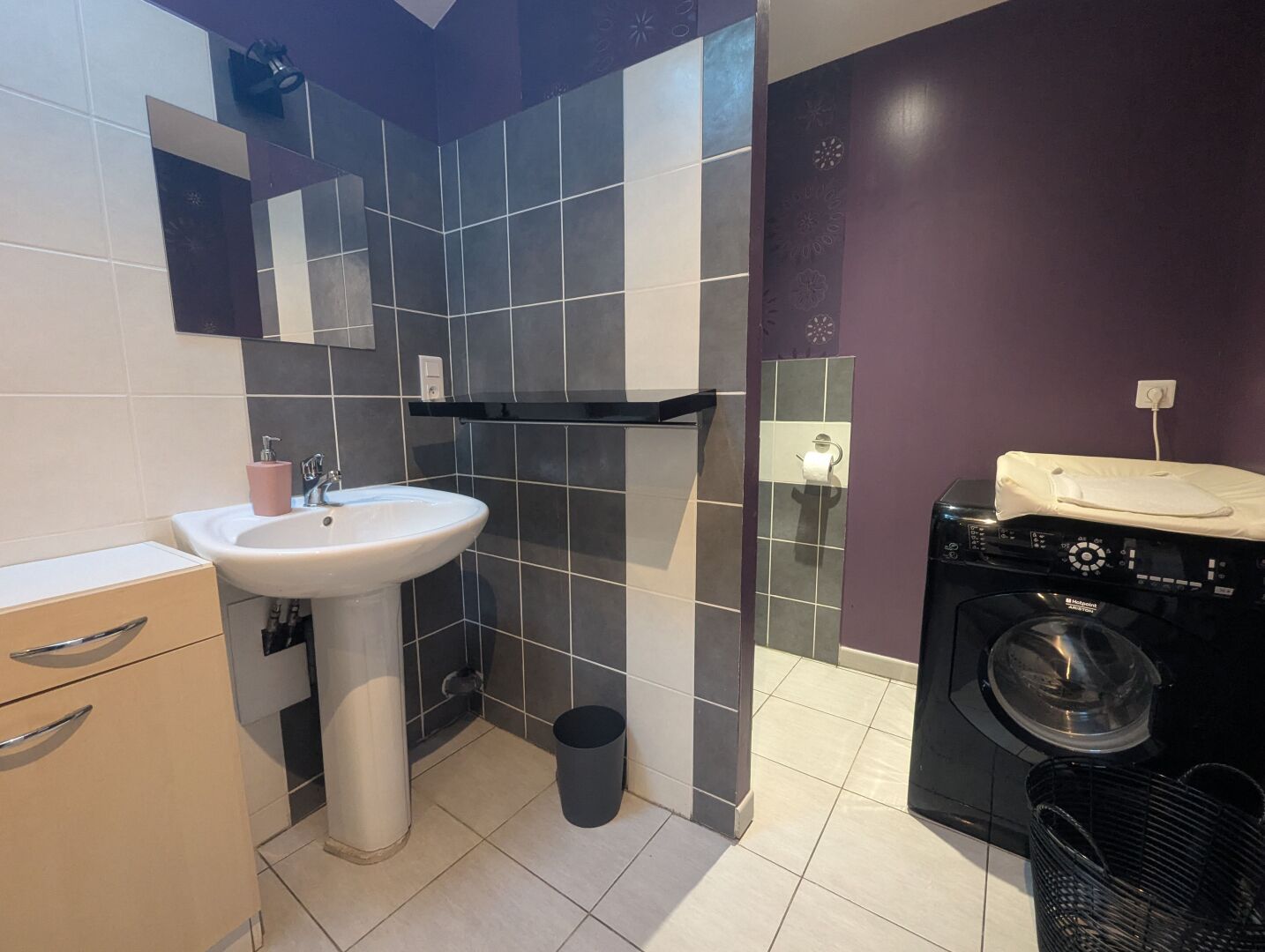 A bathroom with a sink, mirror, towel rack, and a washing machine.