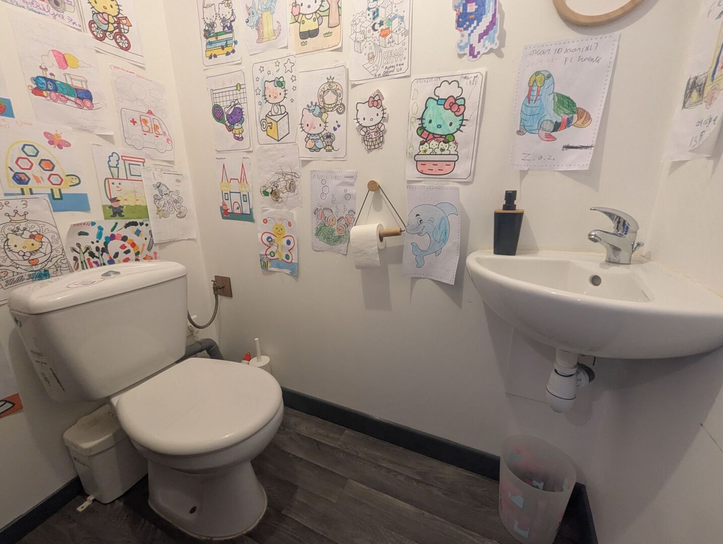 A bathroom with a toilet, sink, and various children's drawings on the walls.