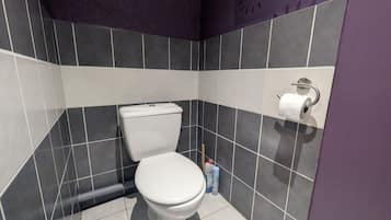 Un bany modern amb un vàter blanc, rajoles grisos fosc i una paret color morat.