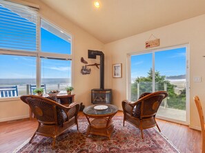 A room with a large window, a fireplace, wicker furniture, and a view of the beach. - Wavewatcher at Nye Beach *Beach Trail*Ocean Views (Newport)