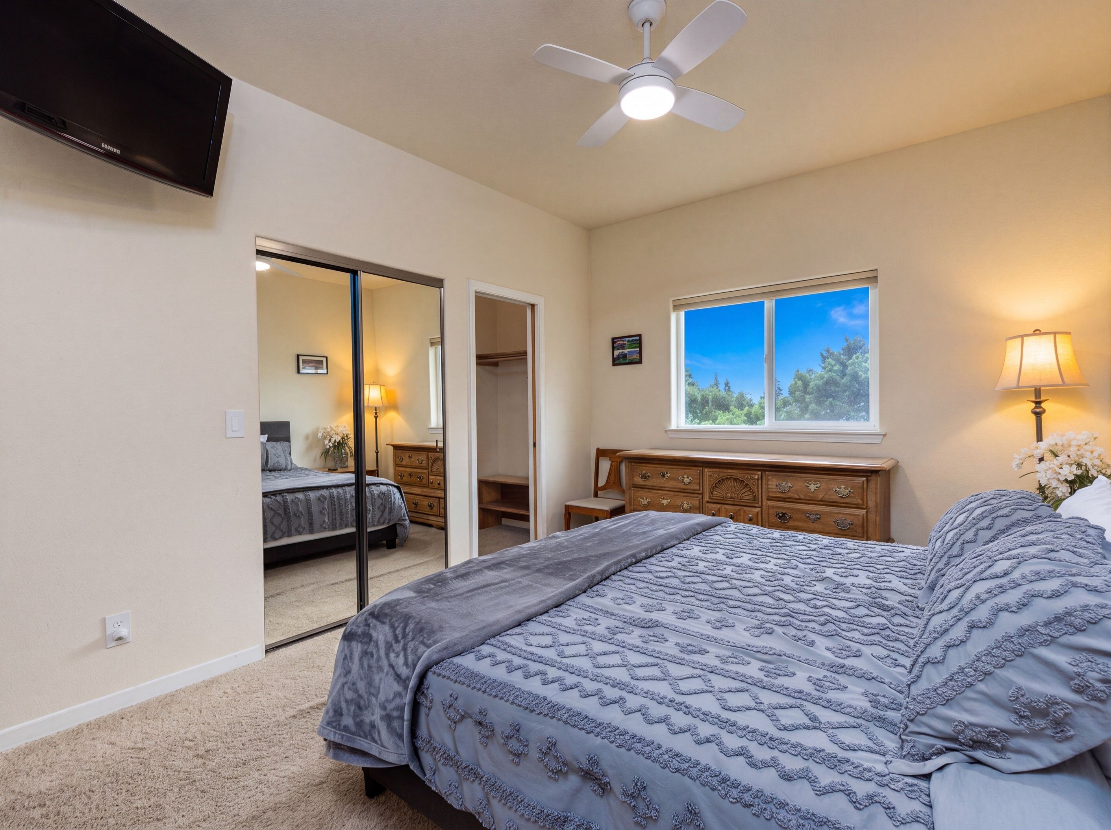 Une chambre à coucher comprenant un lit, une commode, une fenêtre avec vue, un ventilateur de plafond et un téléviseur fixé au mur.