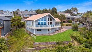 Une maison à deux étages dotée d’un balcon, entourée d’une végétation luxuriante et d’autres immeubles résidentiels.