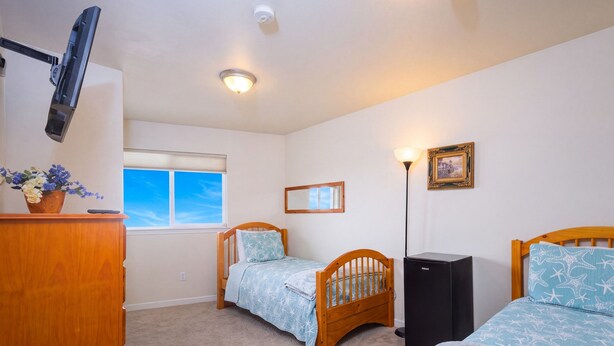 Une chambre avec deux lits en bois, un bureau avec un ordinateur, une fenêtre donnant sur un beau paysage et un luminaire au plafond.