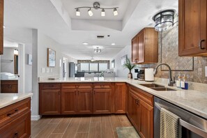 A modern kitchen with wooden cabinets, a marble countertop, and a built-in dishwasher. - Floridian Paradise - Luxury Oceanfront Condo (Daytona Beach Shores)