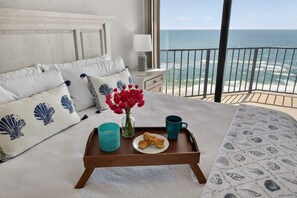 A bedroom with a bed, pillows, a tray with pastries, a vase of flowers, a mug, and a view of the ocean. - Floridian Paradise - Luxury Oceanfront Condo (Daytona Beach Shores)