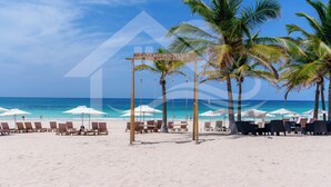 Ein Strand mit Liegestühlen und Sonnenschirmen, ein Schild für "Cana Bay Beach Club" und Palmen.