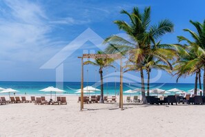 Ein Strand mit Liegestühlen und Sonnenschirmen, ein Schild für 'Cana Bay Beach Club' und Palmen.