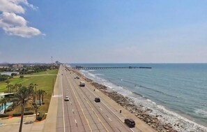 Eine Küstenstraße mit Fahrzeugen, einem Strand und einem Pier in der Ferne.