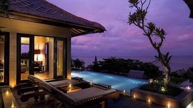 Zona junto a la piscina con sillones de descanso y velas, con vistas a un cuerpo de agua.