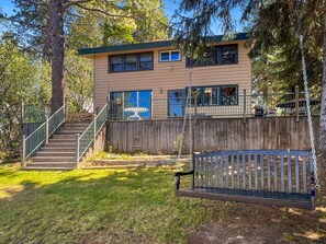 A two-story building with a wooden deck, a staircase, and a swing bench. - Payette Lake Retreat | Dock, Beach, Room for Toys! (McCall)