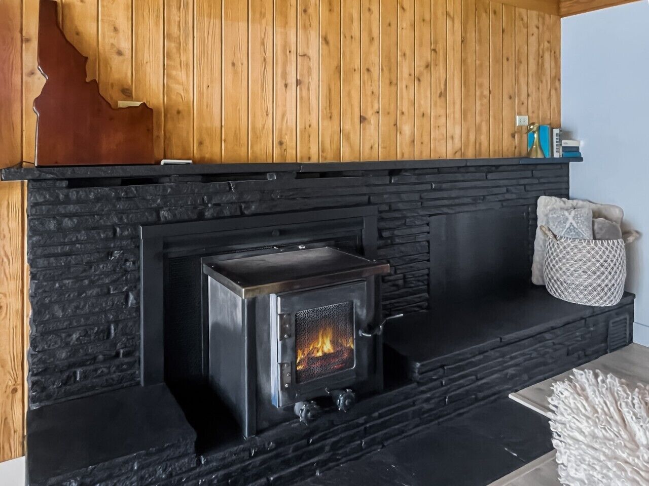 A wood-burning stove in a fireplace, a wooden wall, and a black stone surround.