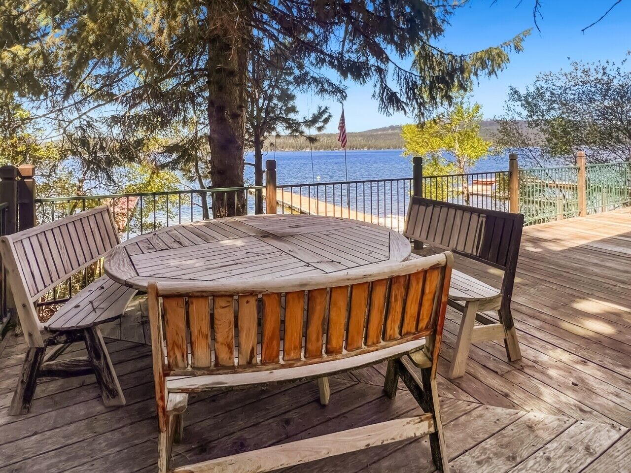 Een houten terras met een ronde tafel en vier banken, uitkijkend op een wateroppervlak.