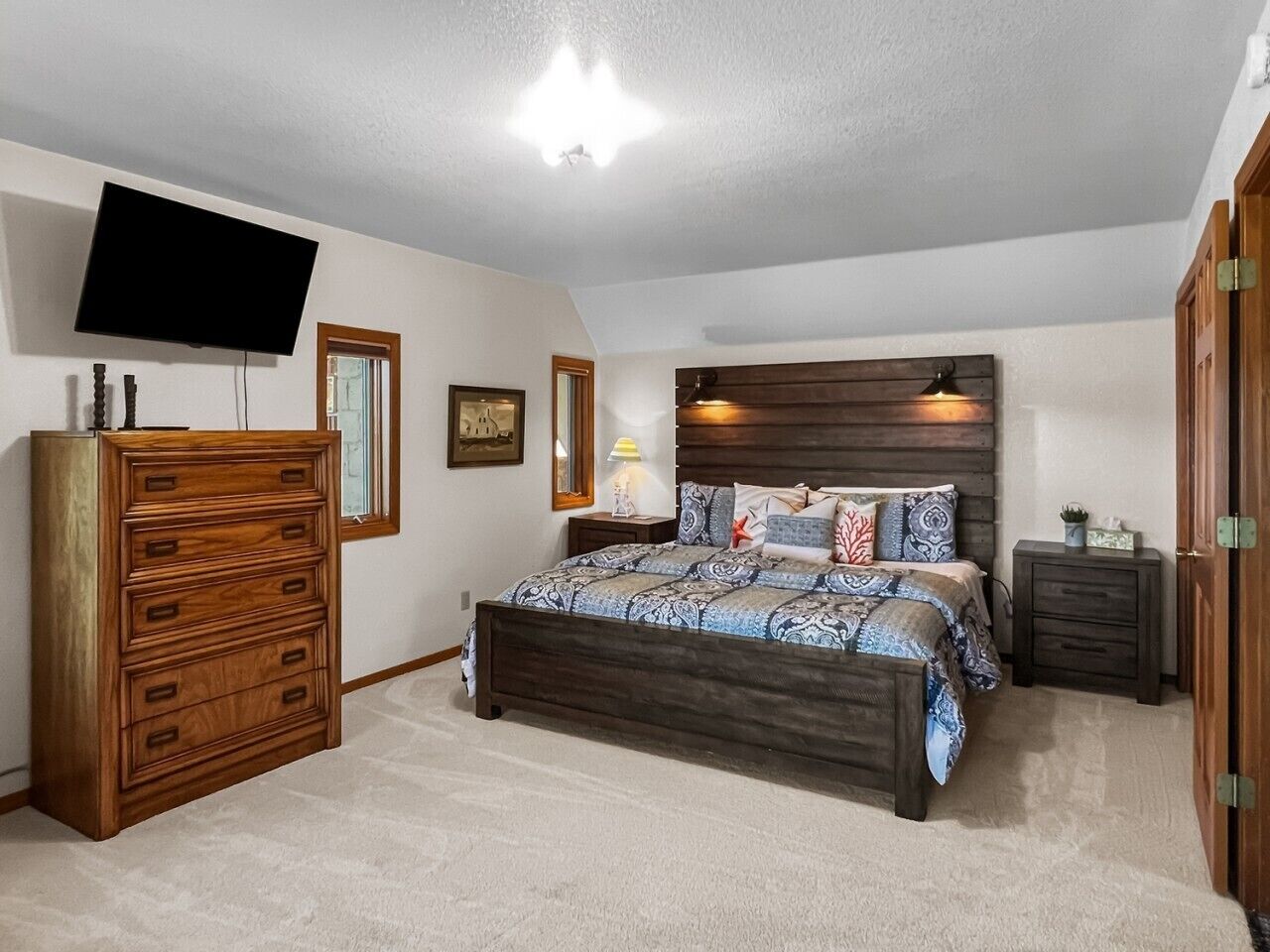 A bedroom with a bed, dresser, nightstand, TV, and a ceiling light.