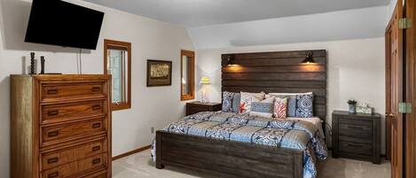 A bedroom with a bed, dresser, nightstand, TV, and a ceiling light.