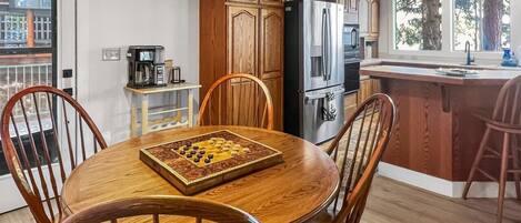 Ein Holztisch mit Stühlen, eine Kaffeemaschine und ein Schachbrett in einer Küche mit Holzausstattung und einem Kühlschrank.