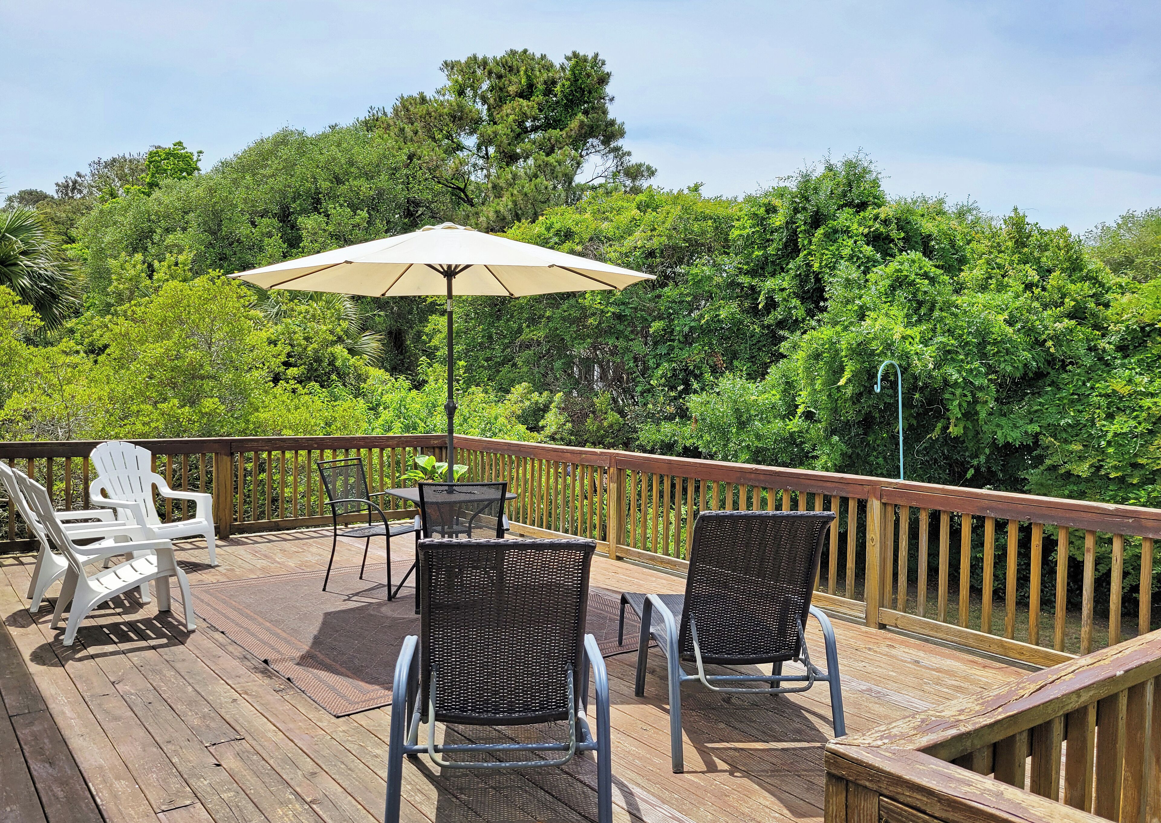 Eine Holzterrasse mit Gartenmöbeln, darunter Stühle und ein Tisch, umgeben von üppigem Grün.