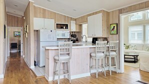 Una cocina moderna con paneles de madera, una isla central con taburetes de bar y un área de comedor con sofá y mesa.