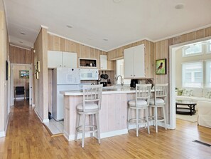 Eine moderne Küche mit Holzvertäfelung, einer zentralen Kochinsel inklusive Barhocker und einem Essbereich mit Sofa und Tisch.