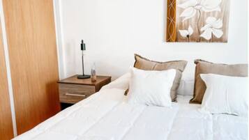 Un letto rifatto con lenzuola e asciugamani bianchi, un comodino in legno con una lampada e un’opera d’arte a parete.