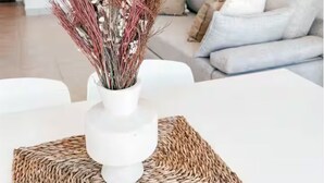 A modern living room with a white table, a woven placemat, and a vase with dried plants. - Dpto ubicación ideal para 6 (Salta)